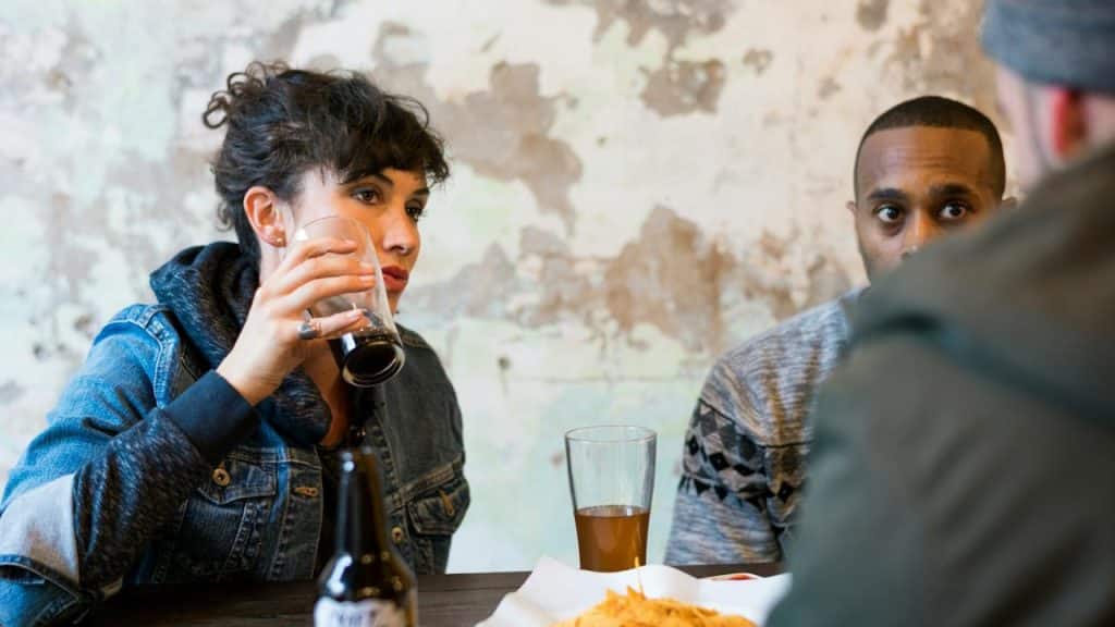 A man and a woman are drinking alcohol at a cafe and another man is looking at them.