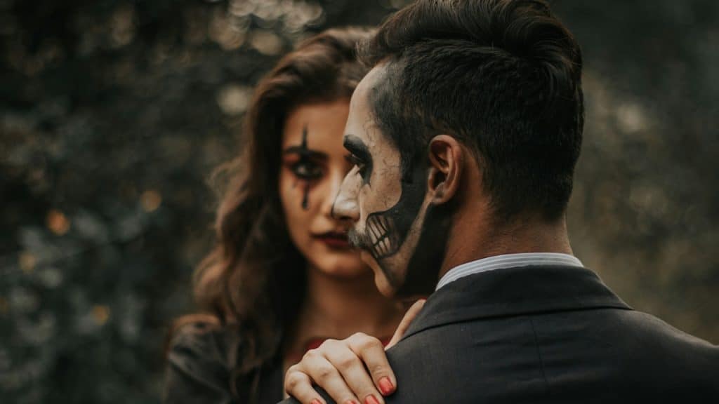 Two people stand close together outdoors, both wearing dramatic face paint.