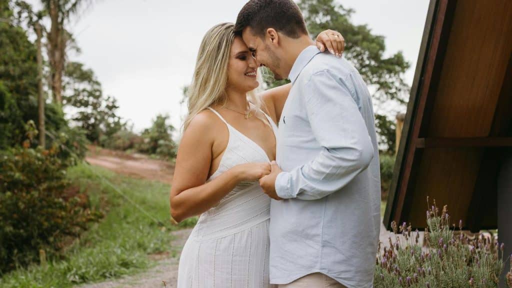 A couple standing close together outdoors, smiling with their foreheads touching.