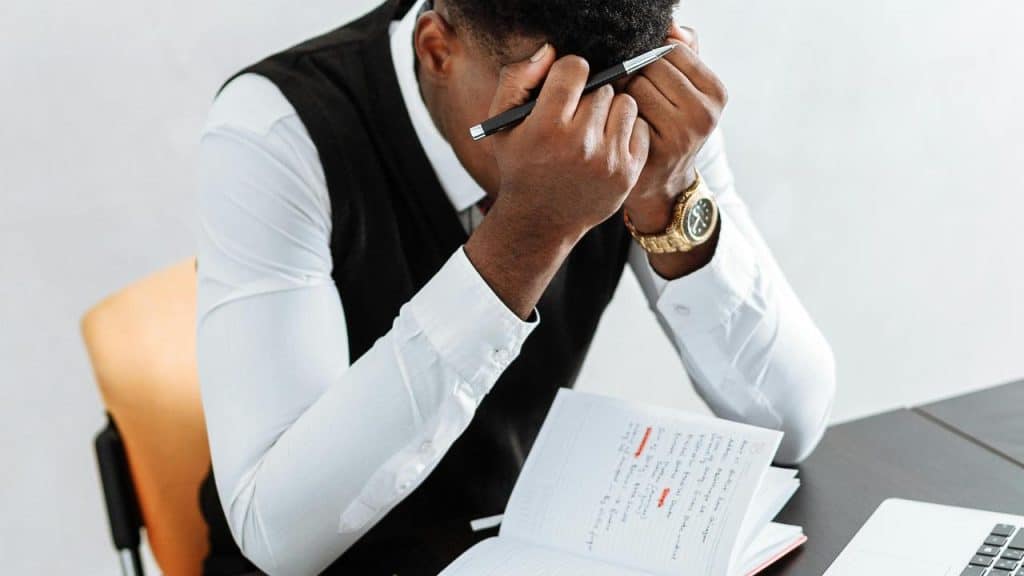 A stressed man sitting at a desk with his head in his hands.