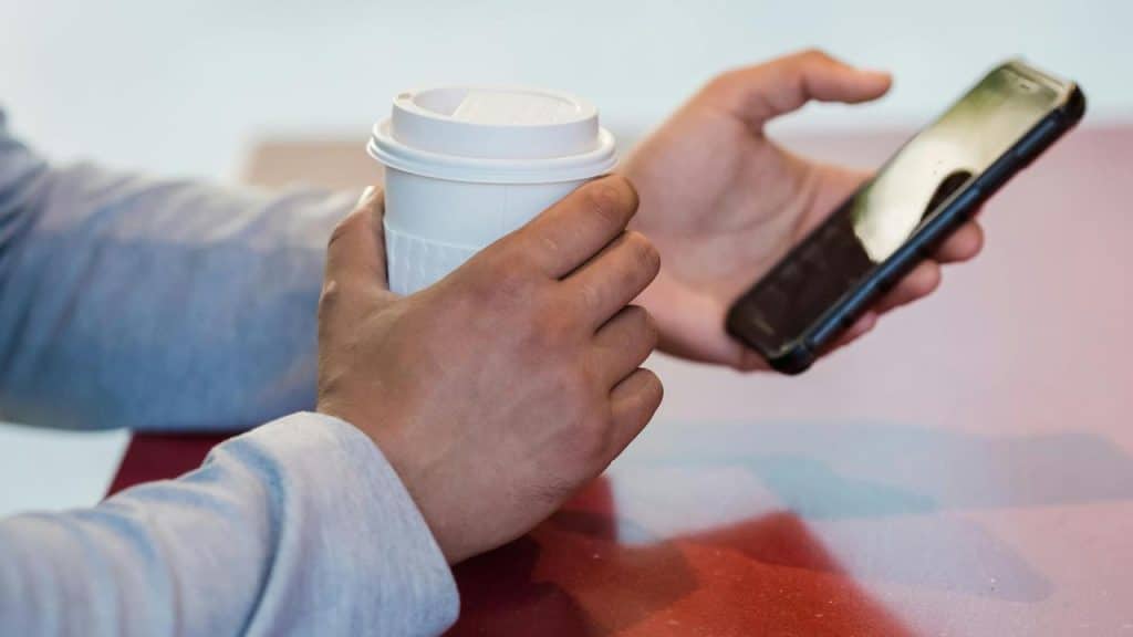 A person holding a coffee cup while using a smartphone.