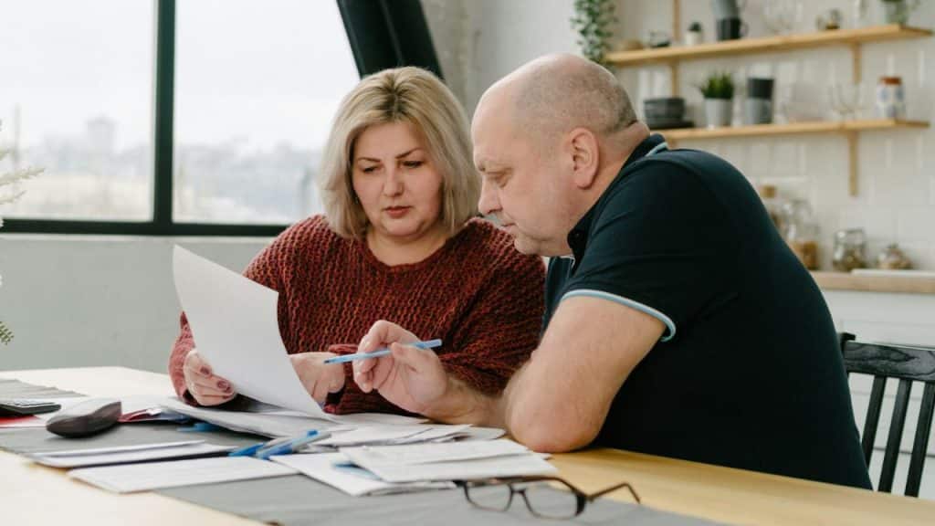 A woman holds a document while a man points at the paper with a blue pen.