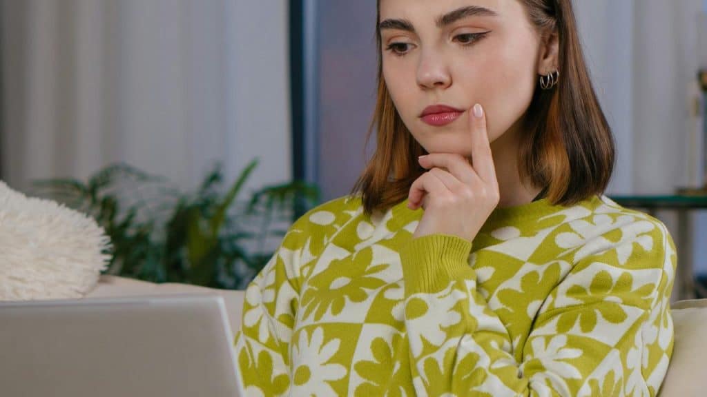 A woman resting her finger on her chin while looking thoughtfully at a laptop.