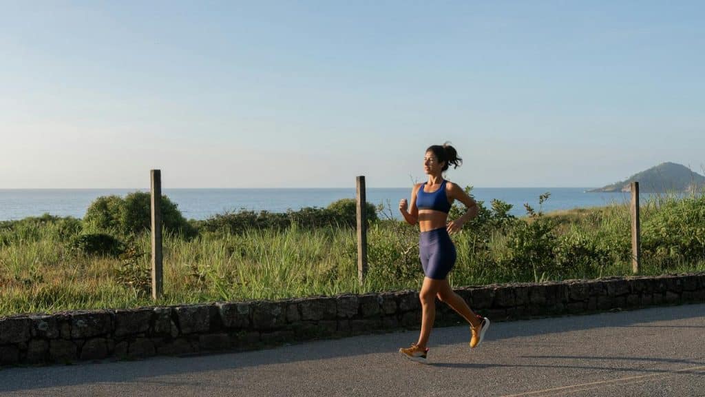 A woman jogging on a road by the ocean.