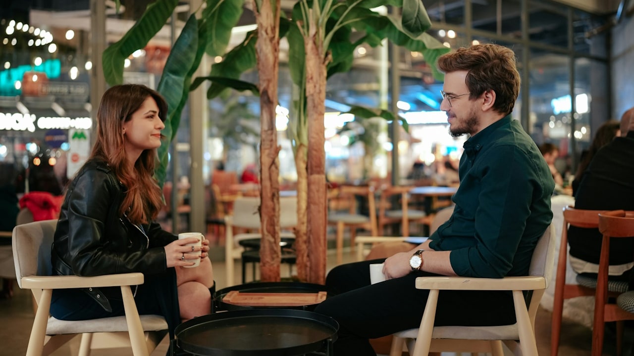 A couple sitting at a table and having coffee while looking at each other.