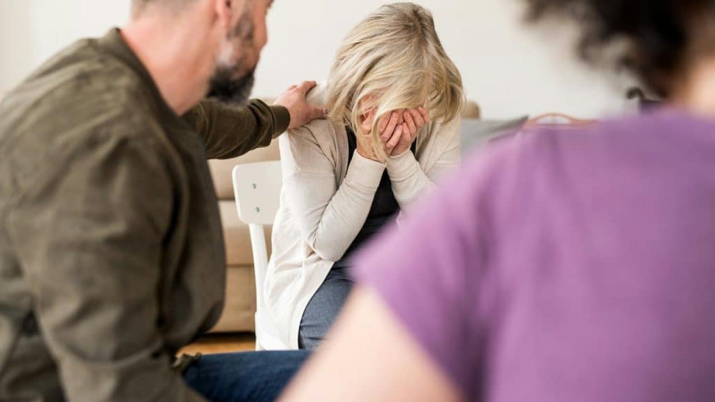 An older woman crying with her face in her hands while someone comforts her.