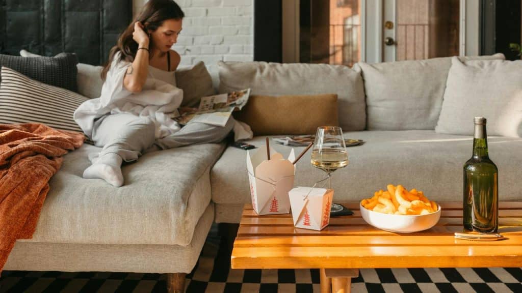 A woman relaxing on a couch while reading, with takeout food and wine on a table.