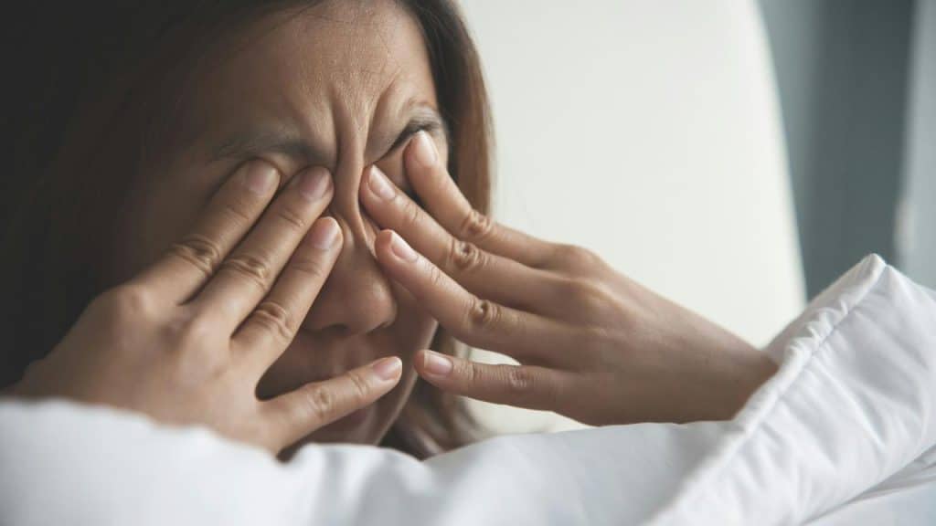A woman lying in bed rubbing her eyes with both hands.