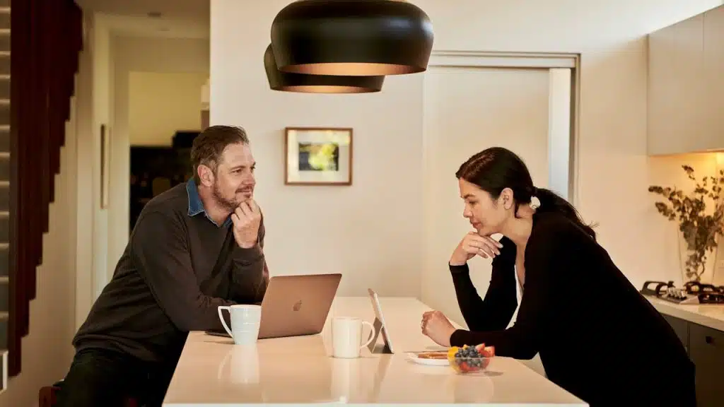 A man and a woman sitting at a table with a laptop and a smartphone.