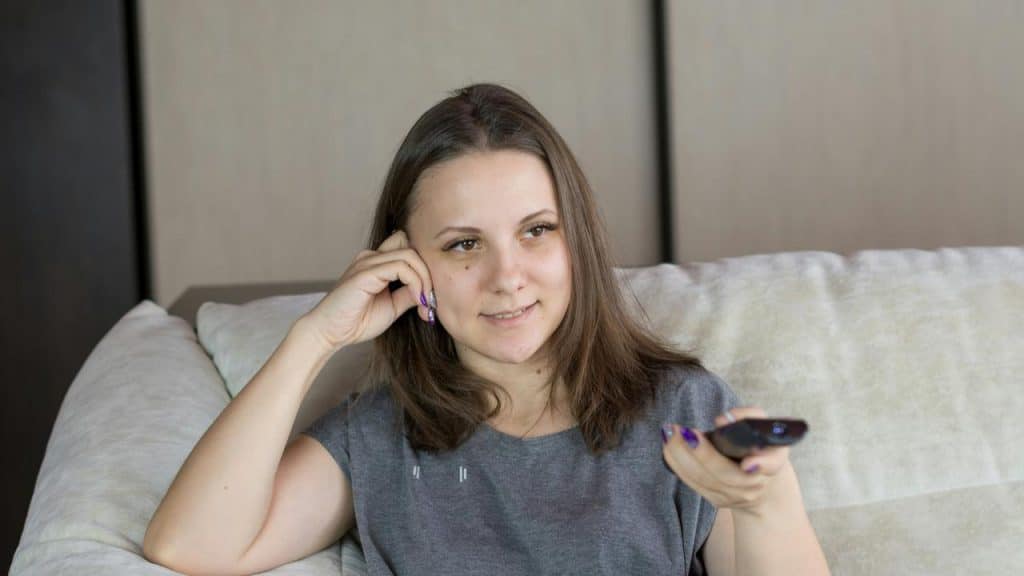 A woman sits on a couch holding a TV remote.