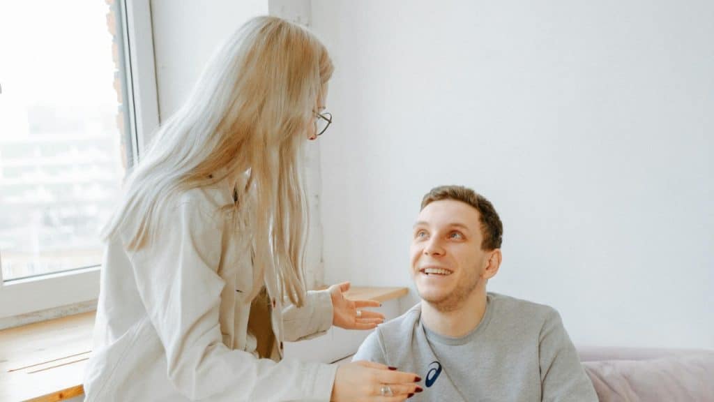 A woman with long blonde hair gestures with her hands while talking to a seated man.