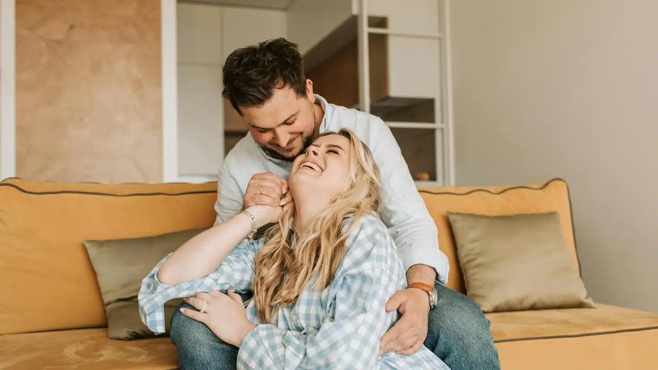 A couple laughing together while sitting on a couch.