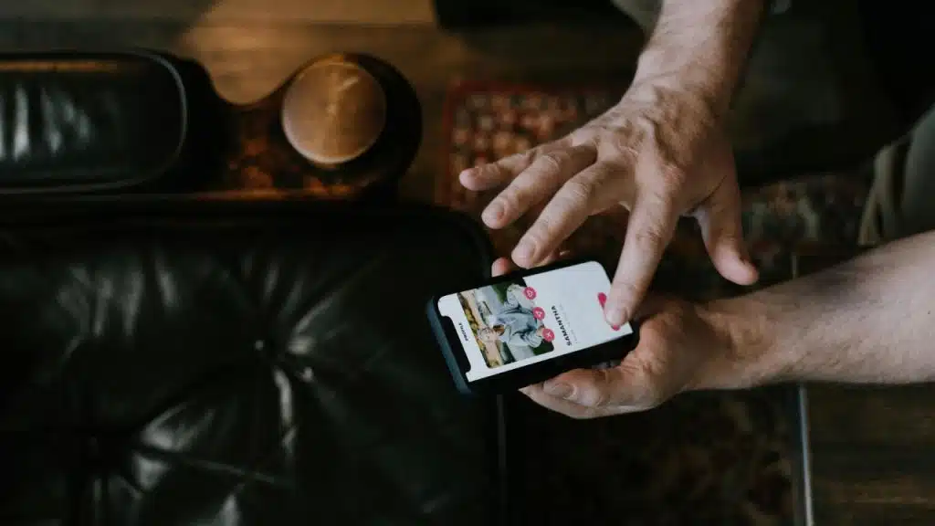 Close-up of hands using a smartphone displaying a digital profile with photos and icons.