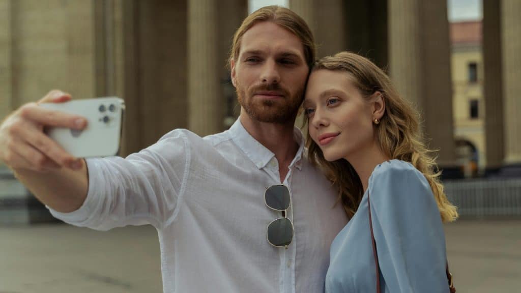 A man holds a smartphone to take a selfie while a woman leans her head.