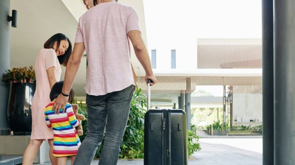 A man pulls a suitcase while a woman and child walk beside him toward a building.