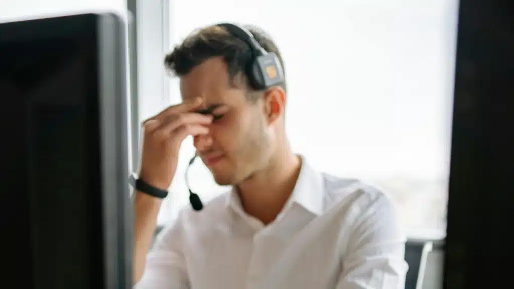 A blurry image of a man wearing a headset with his hand on his face.