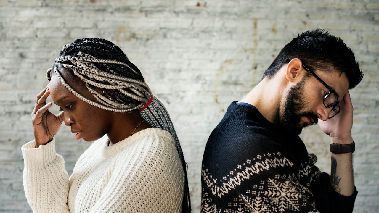 A man and woman standing back-to-back, both holding their heads.