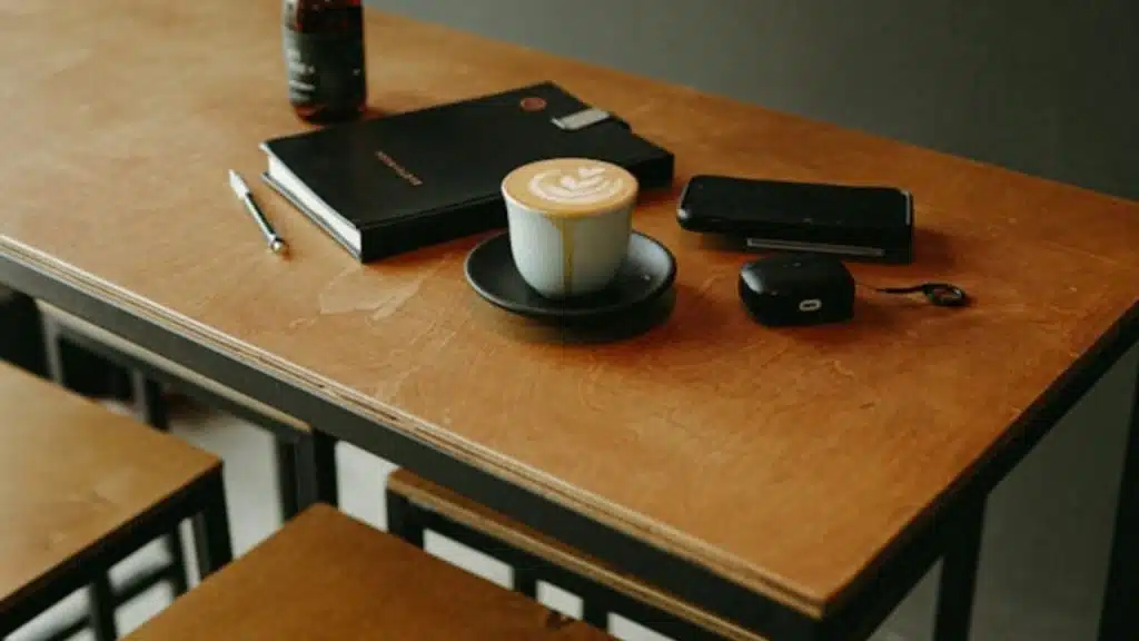 A cup of latte and a smartphone sit on a wooden table next to a notebook.