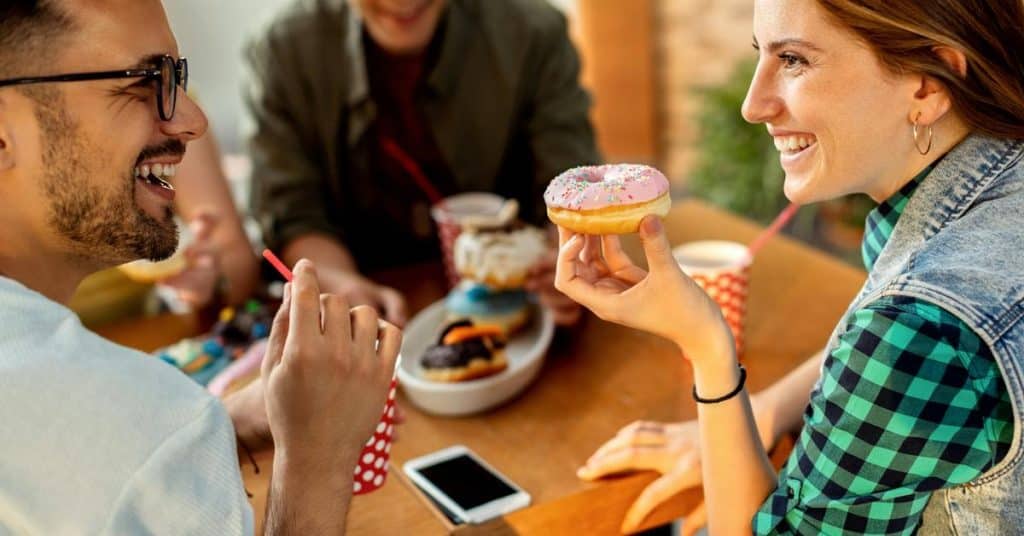 A group of friends laughing and sharing donuts at a café table.