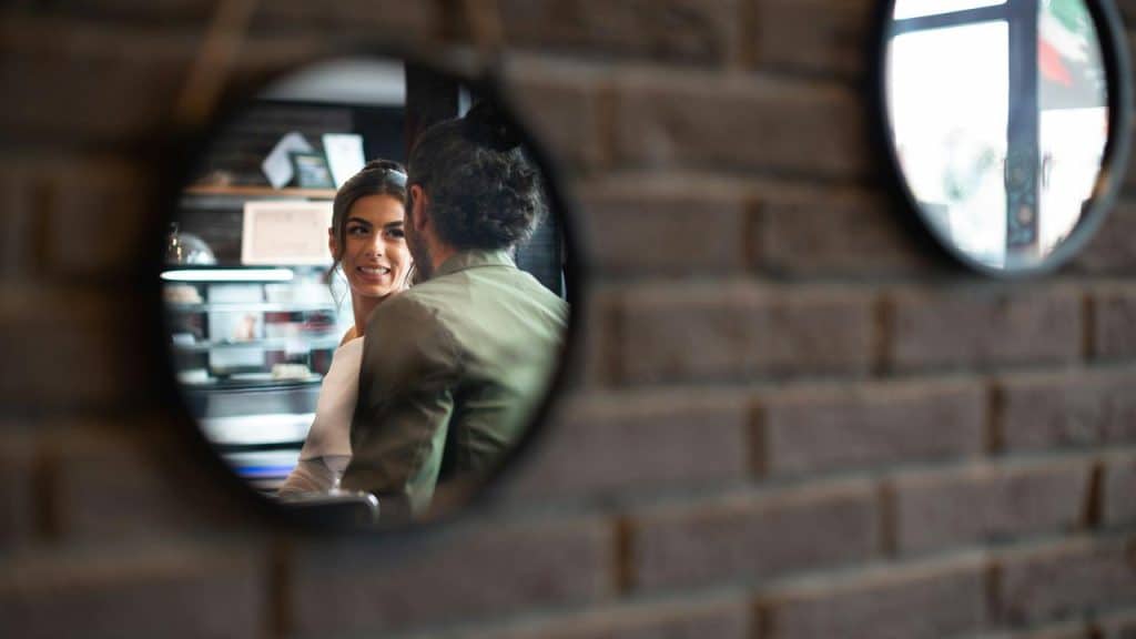 A couple talking in a café, seen through a round mirror on a brick wall.