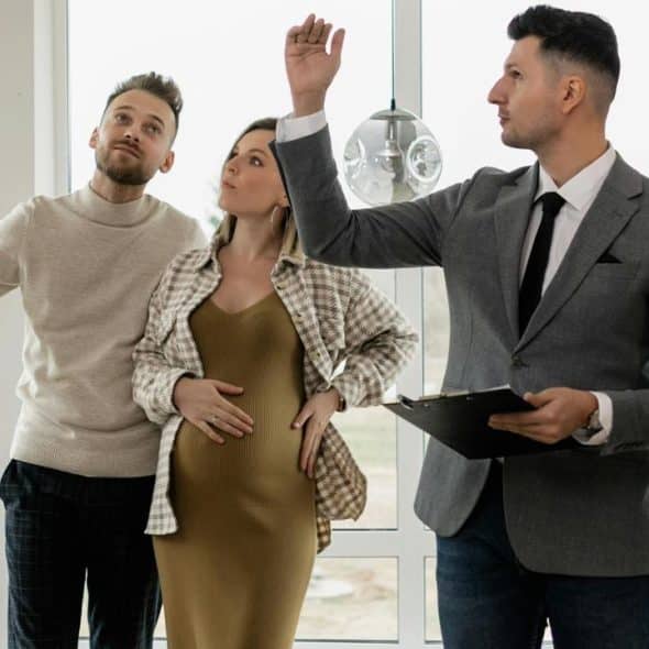 A couple touring a home with a real estate agent holding a clipboard.