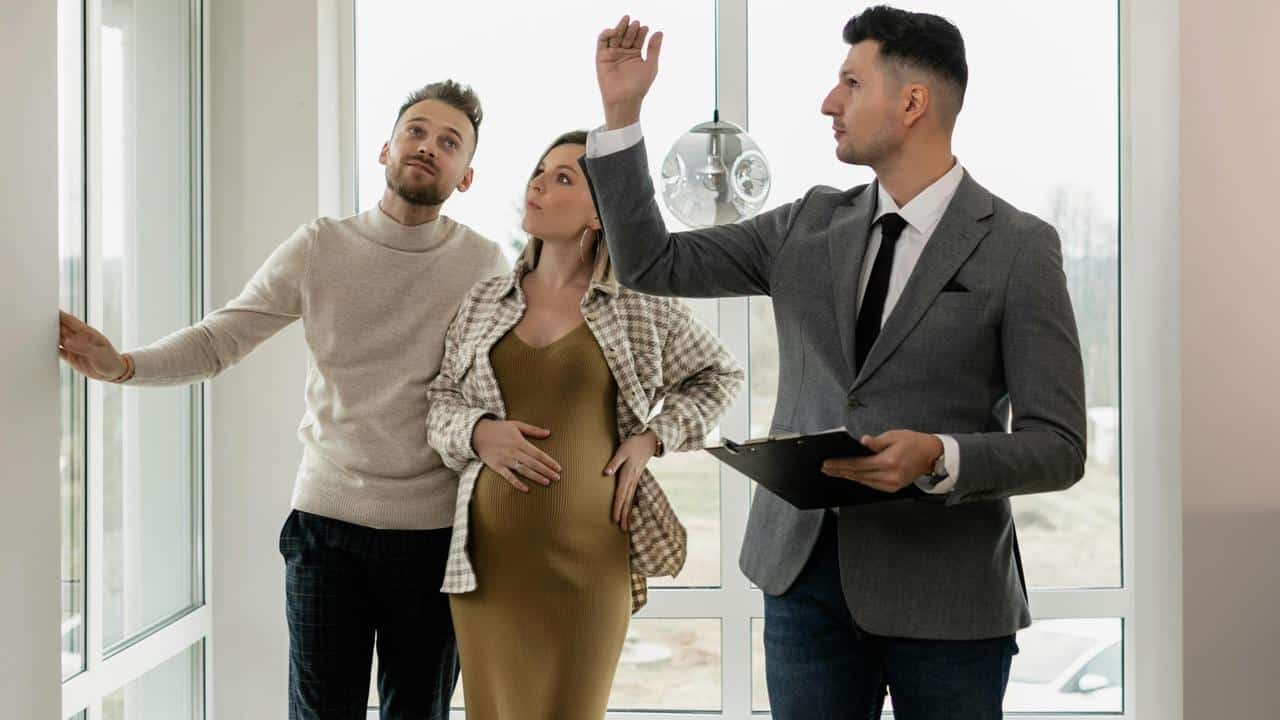 A couple touring a home with a real estate agent holding a clipboard.