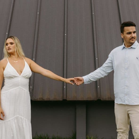 A couple standing apart while holding hands and looking in opposite directions.