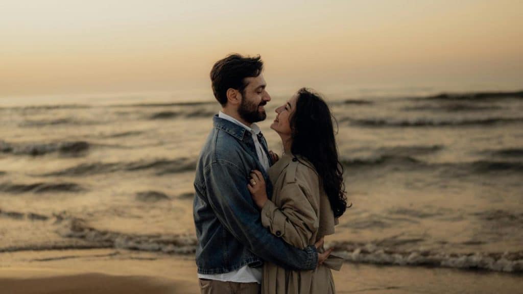 A couple embracing and smiling at each other on a beach at sunset.