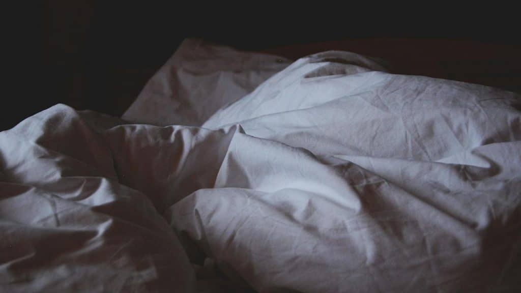 A bed with messy white sheets in dim lighting.