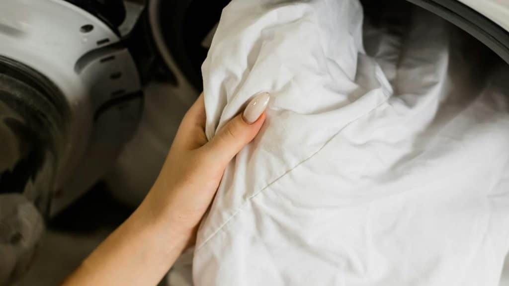 A person's hand holding white laundry in front of a washing machine.