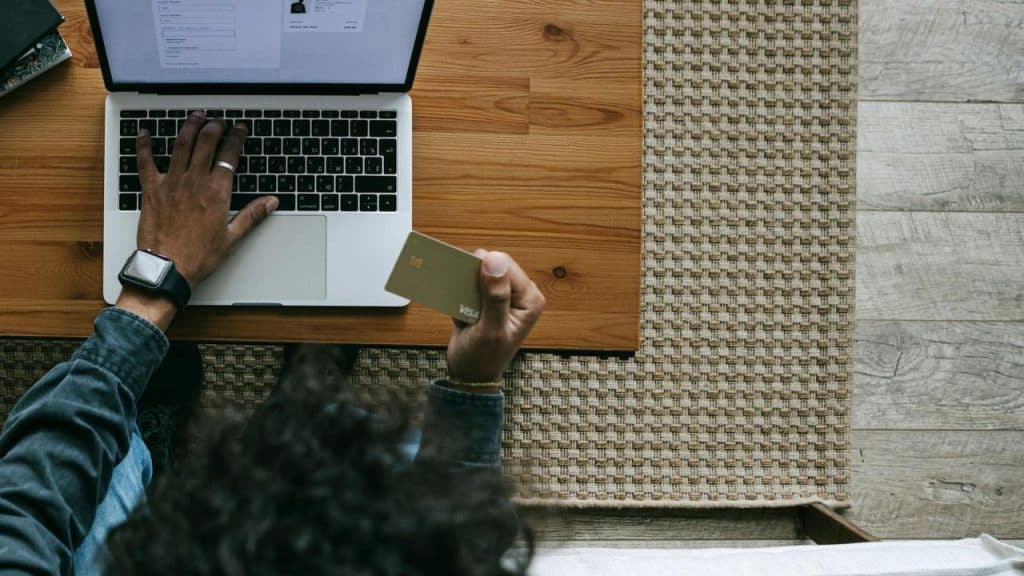 Overhead view of a person using a laptop while holding a gold-colored credit card.