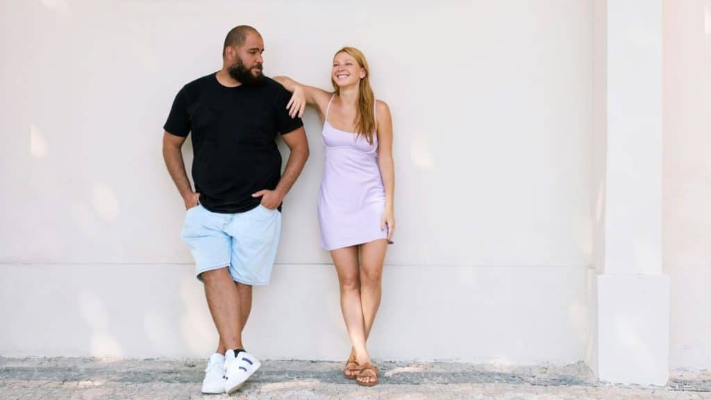 A woman in a purple dress leans her elbow on the shoulder of a bearded man.