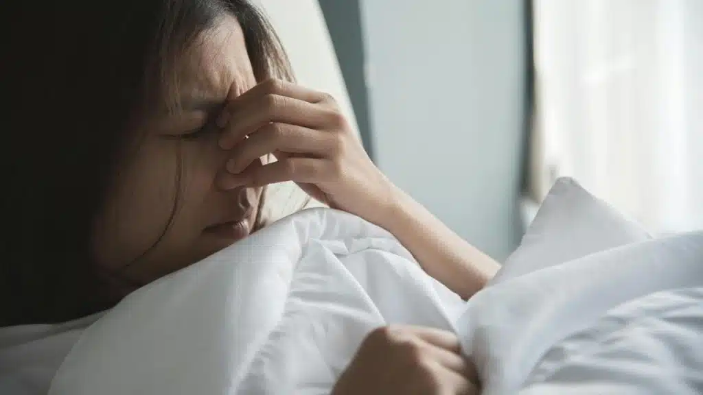 A tired woman in bed holding her face as if in pain or stress.