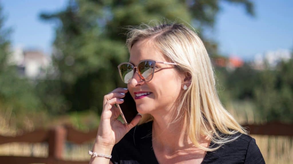 An older woman wearing sunglasses and speaking on the phone.