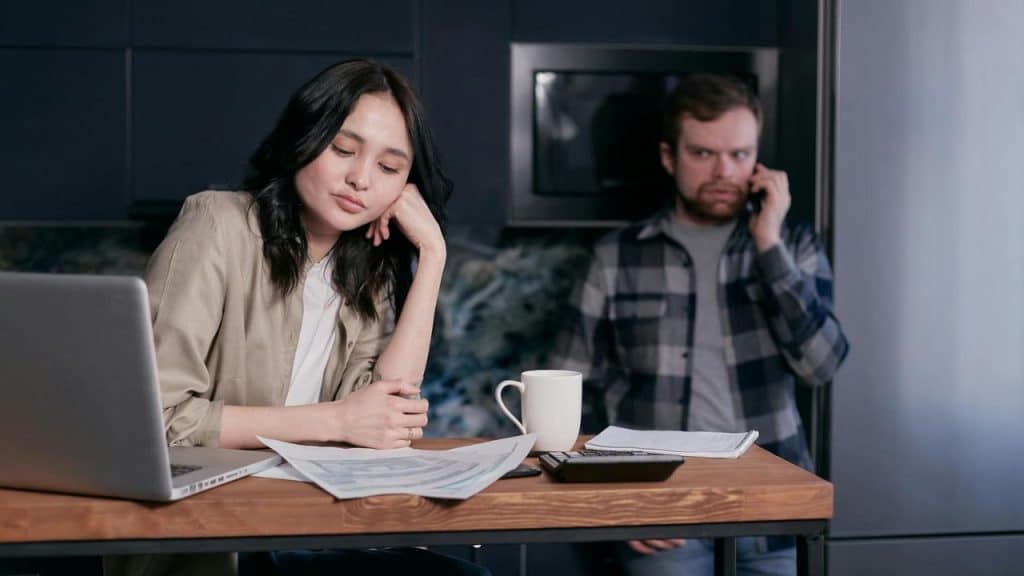 A woman leans on her hand over papers while a man talks on a phone.
