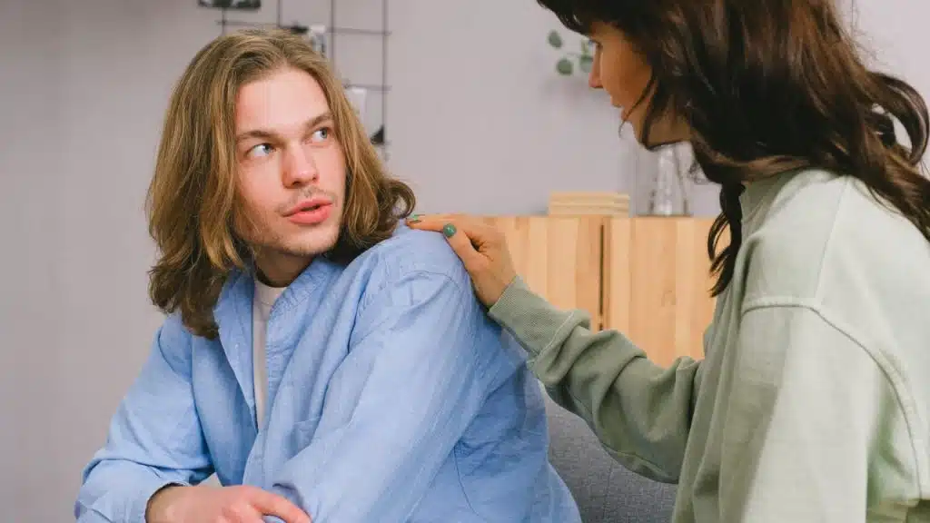 A woman places her hand on a man’s shoulder as they look at each other.