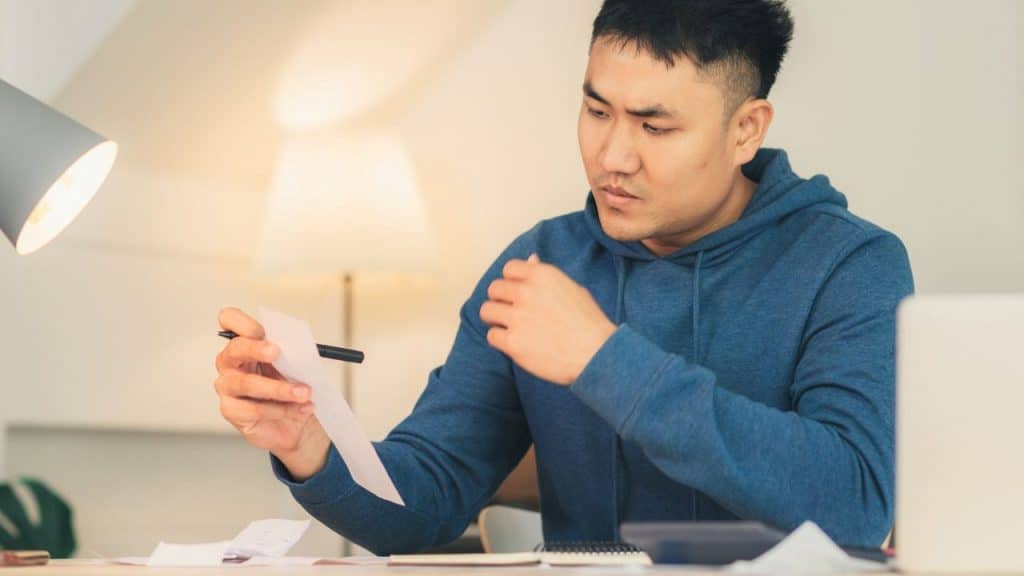 A man in a blue hoodie looks at a piece of paper while holding a pen.