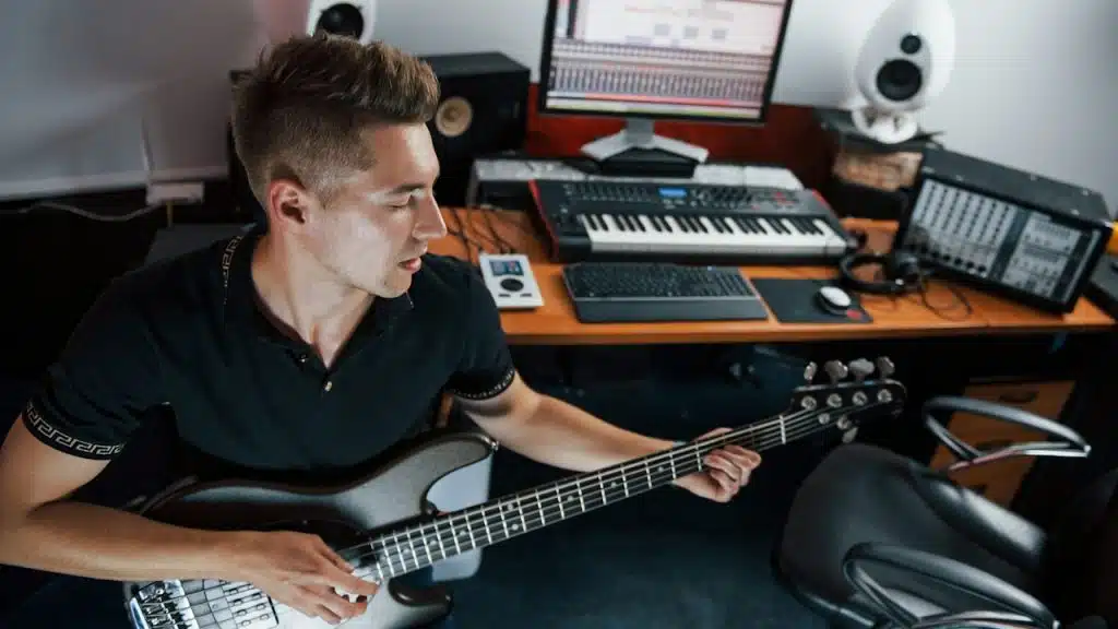 A man is playing a guitar while some musical equipment can be seen on a table behind him.