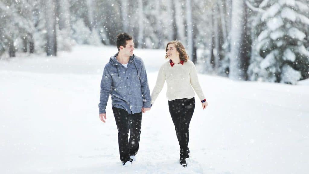 A couple walking on snow near trees during daytime.