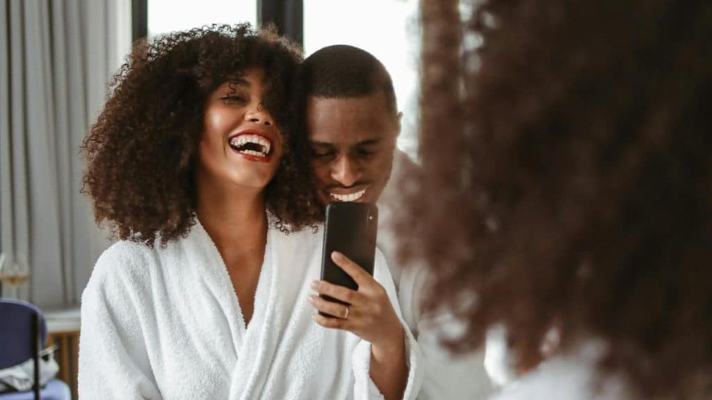A couple in bathrobes laughing and taking a selfie together.