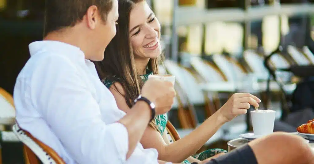 A couple smiling and enjoying coffee together at an outdoor café.