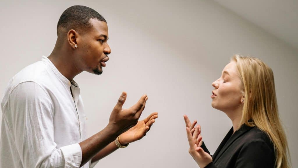 A man and a woman stand facing each other while gesturing with their hands during conversation.