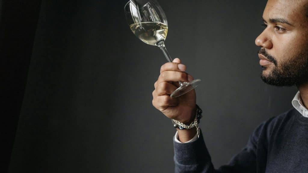 A man holding up a wine glass and examining the white wine.