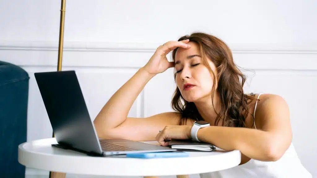 A tired woman resting her head near a laptop at a table.