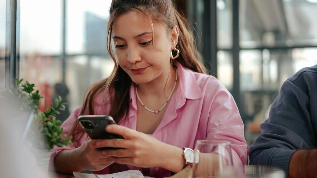 A woman looking at her phone while seated at a table indoors.