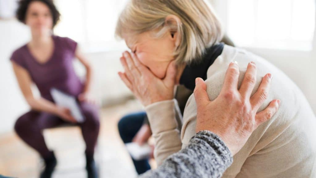 An older person covers their face while another person offers comfort them.