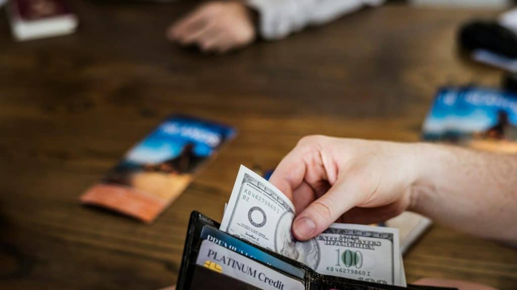 A person's hand holding a wallet with credit cards and a hundred-dollar bill.