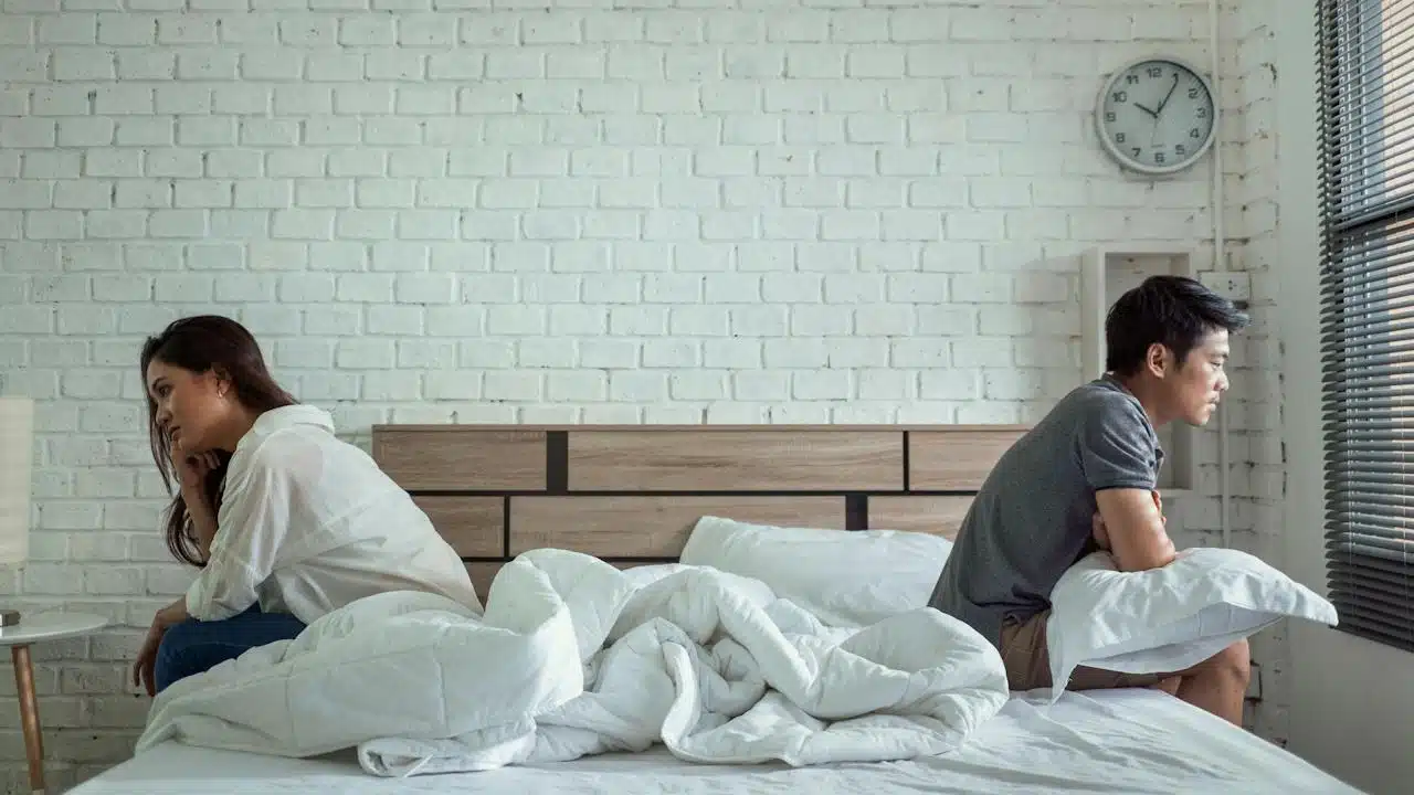 A couple sitting apart from each other on a bed with their backs to each other.