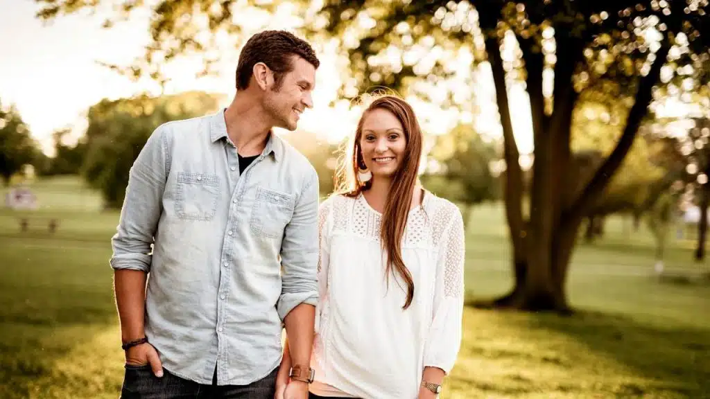 A man looking at his wife while they are standing in a park.