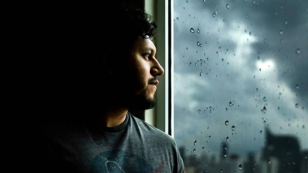 A man gazing out a rainy window with a thoughtful expression.